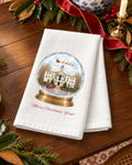 Merry Christmas, Y'all! snow globe tea towel styled in a holiday scene, showing the Oxford courthouse inside a snow globe with Santa's sleigh and a red truck.